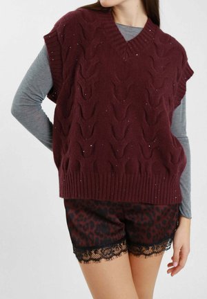 Gilet lavorato a maglia color bordeaux con scollatura a V, caratterizzato da un motivo a trecce e un leggero luccichio. Abbinato a pantaloni corti neri con stampa leopardata e rifiniture in pizzo.