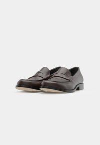 Brune skinnloafers med lav hæl, med et sømt design og en glatt tekstur. Sålen er lysfarget.