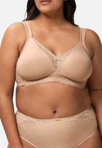 Bežová podprsenka s krajkovým lemováním, nastavitelnými ramínky a strukturovaným designem. Má výstřih do V a decentní mašličku ve středu.