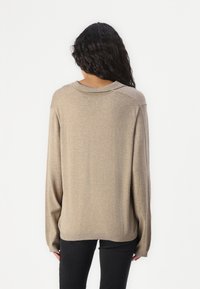 Maglione over-size beige realizzato in morbido tessuto, con scollatura rotonda e spalle abbassate, dotato di maniche lunghe e orlo a coste.