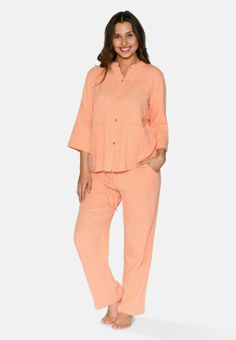 Licht perzik twee-delige lounge set van textuurstof. De top heeft een kraag, knoopsluiting en zakken; de broek heeft een verstelbaar trekkoord.