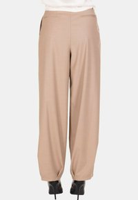 Pantaloni beige a gamba larga con tasche a filetto posteriori indossati con scarpe nere con tacco alto, mostrati di spalle su uno sfondo neutro.