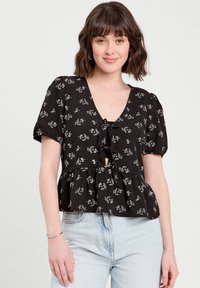 Chemisier noir à motif floral avec un décolleté en V, des manches bouffantes courtes et un détail à nouer à l'avant, comportant un ourlet peplum.