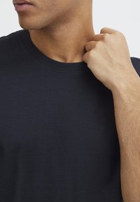 Tricou în nuanță închisă de navy, cu guler rotund cu nervuri. Țesătura pare netedă și aspră, cu un croi ajustat și fără motive vizibile.