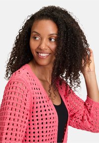 Cardigan en tricot rose avec un motif de mailles ouvertes, design en V et manches longues. La texture est légère et respirante.