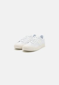 White sneakers made of smooth synthetic material with a low-top design, round toe, and flat rubber outsole. Features lace closure and side logo.