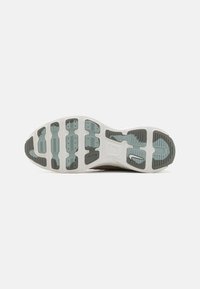 Semelle d'une basket avec une bande de roulement en caoutchouc segmentée en bleu clair et gris, présentant un petit logo Nike swoosh blanc et noir.
