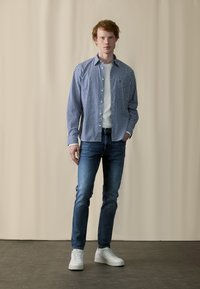Blå og hvit rutete skjorte over en hvit t-skjorte, kombinert med mørkejeans og hvite joggesko. Glatt stoff og avslappet passform.