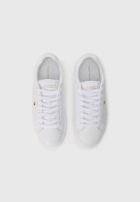 Sneakers bianchi in pelle con finitura testurizzata, caratterizzati da lacci piatti, un marchio dorato sulla linguetta e sottili accenti del logo sui lati.