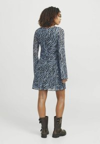 Vestido de manga larga con estampado de cebra en azul y negro, con una cintura ajustada y falda acampanada. Combinado con botas de combate negras de suela gruesa.