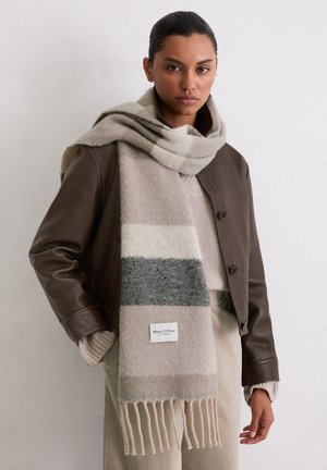 Beige-grau gestreifter Schal aus weicher Wolle, mit Fransen an den Enden und einem Logoelement, getragen über einer braunen Lederjacke.