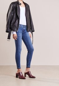 Černá kožená moto bunda, bílý top, modré slim džíny a vínové otevřené sandály na podpatku s robustní patou. Hladké textury a přiléhavý střih.