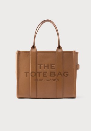 Brūna ādas tote soma ar vertikālām šuvēm, divām noapaļotām rokturiem un iegravētu tekstu: "THE TOTE BAG MARC JACOBS" priekšpusē.