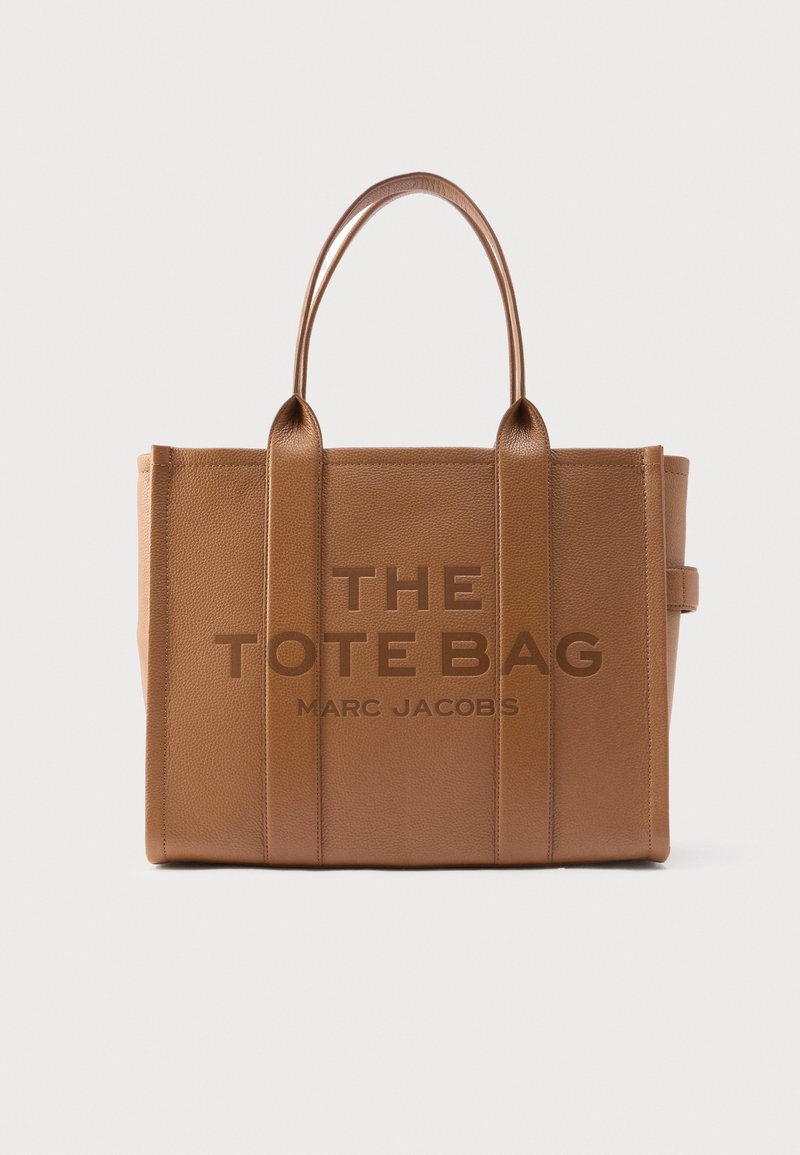Geantă tote maro din piele cu cusături verticale, două mânere rotunjite și text embossat: „THE TOTE BAG MARC JACOBS” pe partea din față.