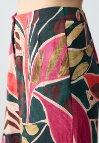 Tessuto colorato e decorato con grandi motivi a foglia in tonalità di rosa, verde e marrone, con una finitura strutturata e un design plissettato.
