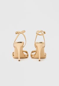 Χρυσά σανδάλια με τακούνι με υφή φίδι, ανοιχτή μύτη, λουριά στον αστράγαλο και τακούνι στιλέτο, με λεία, γυαλιστερή επιφάνεια.