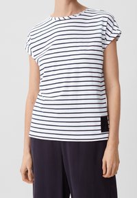 Camiseta de rayas blancas y marino con mangas cortas, cuello redondo y un pequeño parche negro texturizado en el lado.