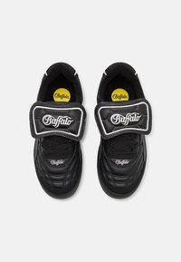 Svarta syntetiska sneakers med vadderad krage, quiltad textur, framträdande kardborreband och vita logotillbehör, med svarta skosnören och gummisulor.