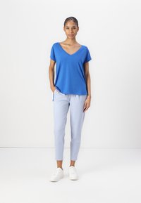 Blå V-hals t-skjorte med korte ermer, kombinert med lyseblå smale bukser og hvite joggesko. Enkel design og myk tekstur.