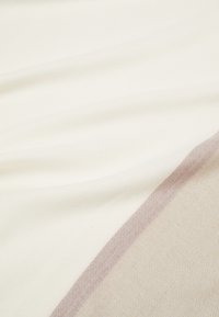 Gros plan sur un tissu doux, plié, blanc et beige avec une subtile rayure diagonale marron clair.