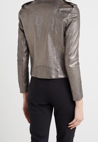 Metallic grijze leren jas met een slim fit ontwerp, schouderepauletten en een gladde textuur, vanachter getoond met een persoon in zwarte broek.
