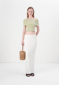 Top corto de canalé verde claro, sin mangas, combinado con una falda maxi blanca texturizada, acompañado de una bolsa de cuerda y sandalias de tacón abierto negras.