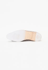 Semelle de chaussure grise texturée avec un fond en caoutchouc blanc lisse, présentant un accent en cuir brun et un détail de logo en relief. Taille 37.