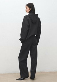 Felpa oversize grigio scuro con cappuccio, abbinata a pantaloni a gamba larga e tacchi neri a punta, con tessuto strutturato e vestibilità comoda.