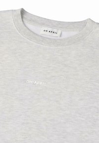 Světle šedá mikina s kulatým výstřihem a žebrovanými manžetami, s bílým vyšívaným nápisem "OH APRIL" na přední straně. Hladký materiál.