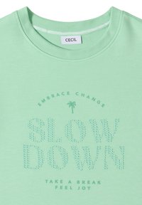 Sweat-shirt vert clair à col rond avec "SLOW DOWN" en points en relief, petit palmier, et phrases "EMBRACE CHANGE" et "TAKE A BREAK FEEL JOY."