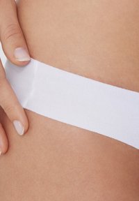 Ceinture élastique blanche de sous-vêtements, texture lisse, vue en gros plan montrant un doigt touchant le tissu contre un teint de peau.