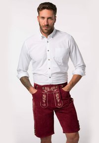 Bordeaux lederhosen lavet af ruskind med dekorativt guld broderi og messingknapper, parret med en hvid skjorte.