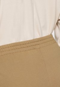 Pantalon élastique beige avec une ceinture côtelée et une texture lisse, présenté avec un haut beige clair.