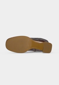 Botte en cuir marron avec bout carré et talon bloc, montrée du côté de la semelle sur fond blanc.