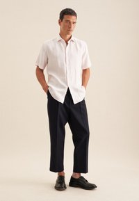 Camicia a maniche corte di un delicato rosa, con una texture sottile, abbinata a pantaloni larghi blu scuro e scarpe in pelle nera. Design semplice e su misura.