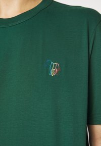 Grünes, kurzärmeliges T-Shirt aus weichem Stoff mit einem mehrfarbigen Pferdedesign, das auf der linken Brust gestickt ist.
