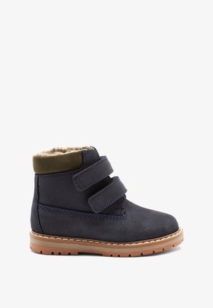 Marineblaue Wildlederstiefel mit einem weichen, hellbraunen Futter aus Fell und olivgrünen Lederakzenten. Verfügt über zwei Klettverschlussriemen und eine Gummisohle.