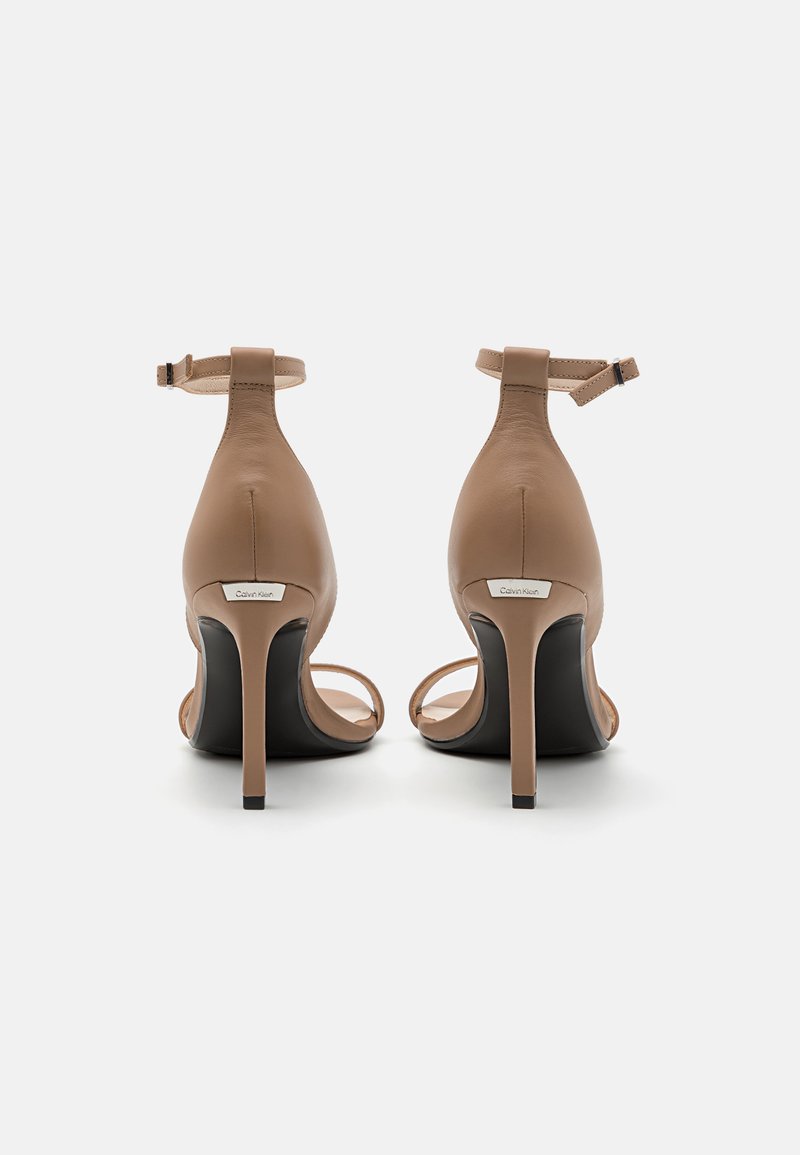 Sandales à talons hauts en cuir beige avec un design à lanières, une bride à la cheville et un fin talon aiguille. Semelle extérieure noire avec un accent de logo minimaliste.