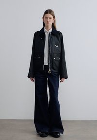 Μαύρο μπουφάν καμβά με μεγάλες τσέπες, ασημένιες μεταλλικές λεπτομέρειες και φερμουάρ μπροστά. Συνδυασμένο με σκούρο καμπανούσες τζιν και μαύρα παπούτσια.