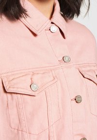 Ljusrosa denimjacka med knappstängning fram, två bröstfickor och silverfärgad metall. Har texturerad tygkvalitet och krage.