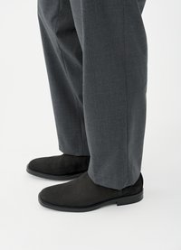 Μαύρα μποτάκια από σουέτ με λεία υφή, στρογγυλεμένη μύτη και χαμηλό τακούνι, συνδυασμένα με ραμμένο γκρι παντελόνι με διακριτικό σχέδιο.