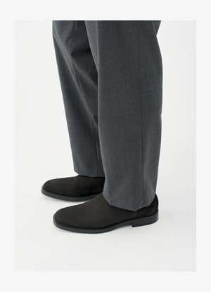 Fekete szarvasbőr boka csizmák sima textúrával, lekerekített orral és alacsony sarokkal, szürke, finom mintás szabott nadrággal párosítva.