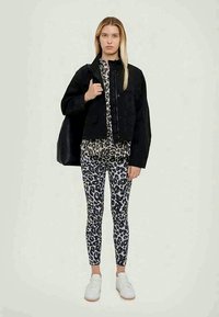 Črna skrajšana jakna, zgornji del z živalskim vzorcem in hlače v črni in beli barvi, kombinirane z belimi superge. Minimalističen dizajn in eleganten videz.
