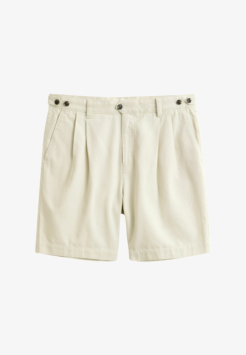 Shorts beige sur mesure avec plis sur le devant, poches latérales, fermetures à boutons à la taille et pattes latérales réglables sur fond blanc.