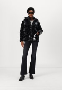 Black shiny puffer jacket with a hood, featuring a geometric quilted design, zipper front, and side pockets. Paired with flared dark jeans.
