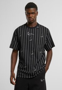 Black short-sleeve T-shirt with vertical white stripes and small bird patterns. Crew neckline and loose fit. Paired with black shorts.