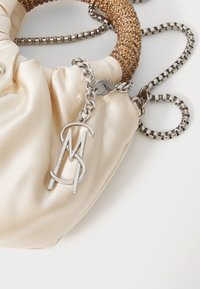Cremefarbene Satin-Handtasche mit einem strukturierten goldenen Griff, silberner Kettenhenkel und einem metallischen Logo-Anhänger. Glatte Oberfläche mit subtiler Schattierung.