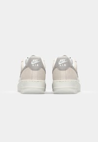 Nike Air sneakers med en beige ruskindsoverdel, grå accenter, hvidt logo og en tekstureret gummisål. Minimalistisk design med en klassisk silhuet.
