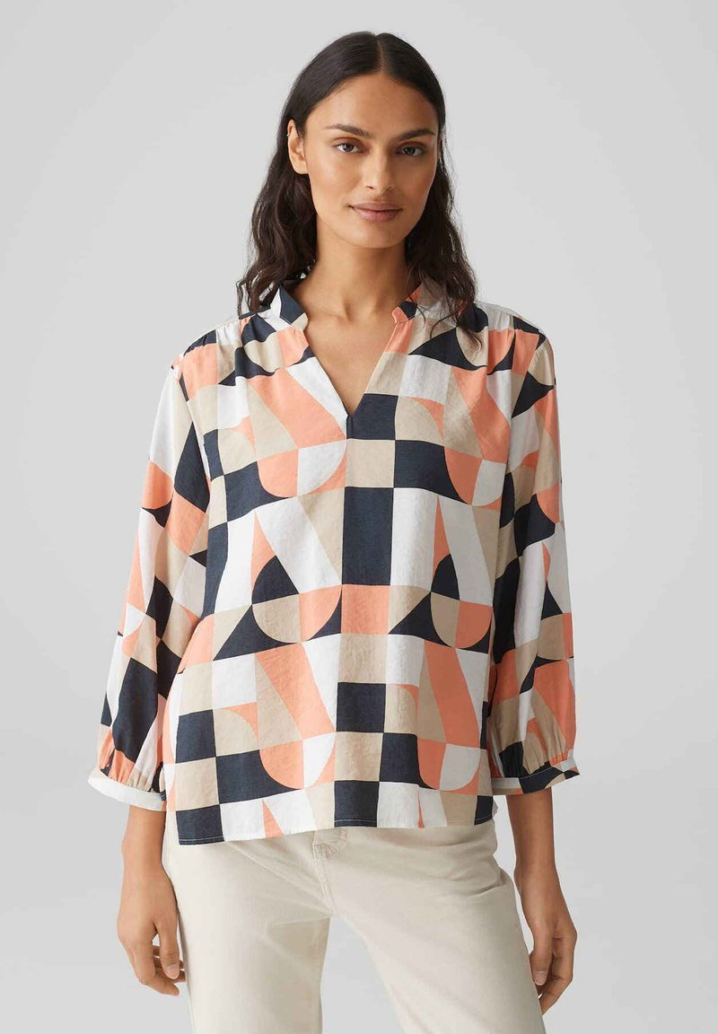 Blusa a maniche lunghe con scollo a V in bianco, blu navy, pesca e beige con motivo geometrico; presenta maniche arricciate e una vestibilità rilassata.