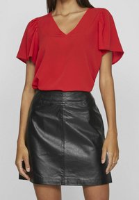 Czerwona bluzka z dekoltem w serek i bufiastymi rękawami, zestawiona z czarną skórzaną mini spódniczką o gładkiej fakturze i szwach na przednim panelu.